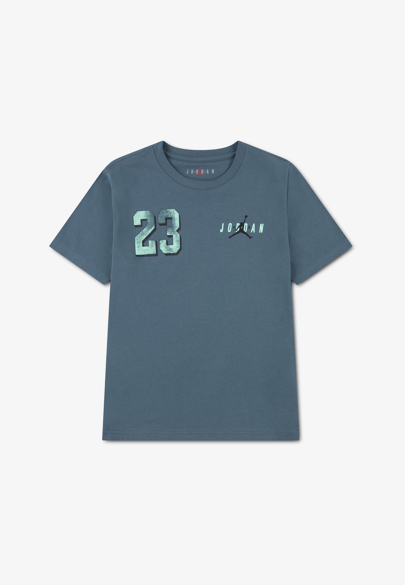 Zils īsroku T-krekls ar metālisku ciparu 23 uz kreisās krūtīm un uzrakstu "Jordan" ar Jumpman logotipu uz labās krūtīm.
