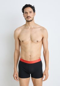 Fekete boxer alsónadrág piros rugalmas derékszíjjal, amelyen a Puma logo látható. Az anyag simának és rugalmasnak tűnik, szorosan simul a testhez.