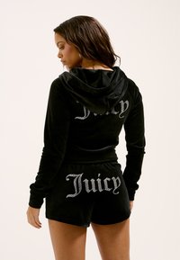 Fekete velúr tréningruha kapucnival. A felső és a rövidnadrág hátulján "Juicy" felirat strasszokkal díszítve. Simogató, luxus érzetet kölcsönző textúra.