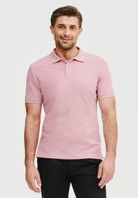 Jasnoróżowa koszulka polo z krótkim rękawem i trzema guzikami. Posiada subtelne logo na lewej piersi. Połączona z czarnymi spodniami.