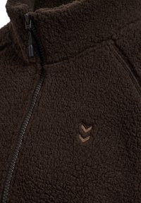 Brun fleecejacka med hög krage, med dragkedja fram. Märkbar textur och broderad logga i en ljusare nyans.