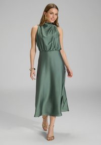 Robe midi en satin vert avec un col haut, une taille froncée et une jupe fluide. Assortie à des talons dorés à lanières et à des boucles d'oreilles accrocheuses.