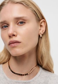 Goldfarbene Ohrringe mit abstrakten geometrischen Formen und einem passenden Choker mit quadratischen Gliedern, der eine Mischung aus Gold- und Schwarztönen aufweist.