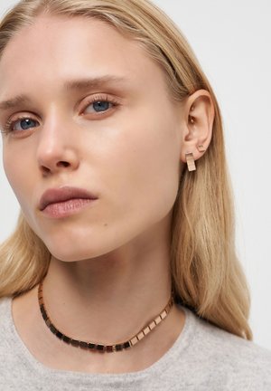 Guldtonade örhängen med abstrakta geometriska former och en matchande choker med fyrkantiga länkar, som har en blandning av guld- och svarta färger.