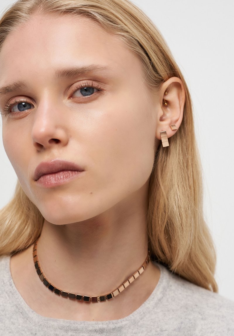 Goldfarbene Ohrringe mit abstrakten geometrischen Formen und einem passenden Choker mit quadratischen Gliedern, der eine Mischung aus Gold- und Schwarztönen aufweist.