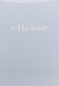 Ljust blå slimmad topp med ribbad textur, med en vit tryckt logotyp "ellesse" på bröstet. Inga ytterligare mönster eller detaljer.