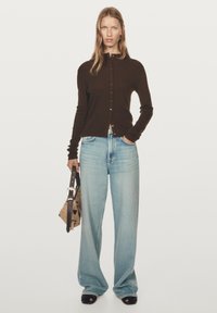 Brown knit cardigan with buttons, paired with light blue wide-leg jeans. The model holds a spotted handbag and wears black platform sandals.