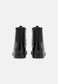 Botas de cuero negro hasta el tobillo con paneles laterales elásticos, punta redondeada, textura suave y tacón bajo apilado. Presenta una cremallera trasera para facilitarn el calzado.