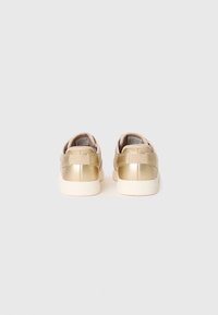 Pair of metallic gold low-top sneakers with beige soles, shown from the back against a plain light gray background.