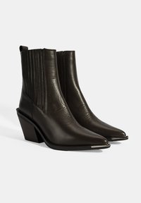 Bottes chelsea en cuir marron foncé avec un bout pointu, une texture côtelée et un talon légèrement surélevé ; ornées d'accents argentés sur le bout.