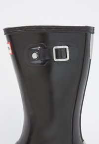 Botte de pluie en caoutchouc noire avec une boucle argentée et un détail de sangle réglable. Texture lisse, forme droite et bord supérieur renforcé.