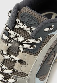 Hallkaad, kus on halli ja musta värvi spordijalats valgete ja mustade mustriliste käiste ning keelal ja külgedel võrgukangaosadega.