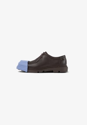 Zapato de cuero marrón con puntera redondeada, que presenta un acento de goma azul en la parte frontal, suela texturizada y detalles de costura.