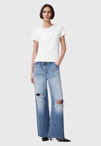 T-shirt bianco a maniche corte con collo a giro, abbinato a jeans a gamba larga di colore blu chiaro con buchi strappati alle ginocchia e orli sfrangiati.