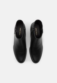 Bottines noires en cuir lisse avec un bout arrondi, dotées d'une fermeture éclair sur le côté et d'accents texturés au niveau du talon.