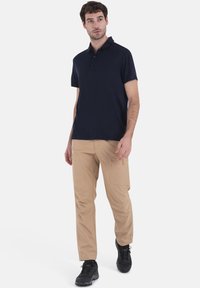 Polo navy con colletto e tre bottoni, abbinato a pantaloni cargo beige chiaro con tasche laterali e scarpe da ginnastica nere.