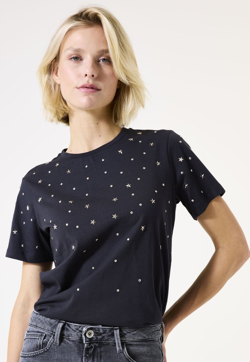 Marineblaues T-Shirt mit verstreuten silbernen Sternen und Paillettenverzierungen, kurzen Ärmeln und einem runden Halsausschnitt. Hergestellt aus weichem Baumwollmaterial.