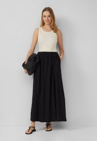 Light cream tank top with ribbed texture, paired with a long black skirt featuring an elastic waistband. Holds a dark knit wrap.