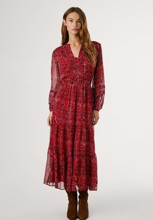 Red long-sleeve maxi dress with floral pattern, v-neck, gathered waist, and layered skirt. Worn with brown ankle boots.
