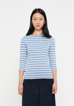 Haut à rayures à manches longues en bleu clair et blanc, en mélange de coton, avec un col rond et un petit logo sur la poitrine. Jupe unie marine.