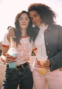 Deux personnes boivent des granités color�és. L'une porte une chemise blanche avec un liseré rouge et des lunettes ; l'autre, un col roulé et une veste en jean.