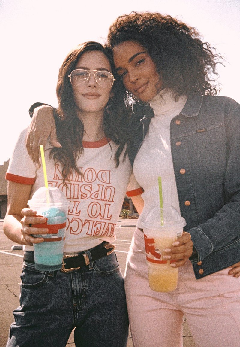 Deux personnes boivent des granités colorés. L'une porte une chemise blanche avec un liseré rouge et des lunettes ; l'autre, un col roulé et une veste en jean.