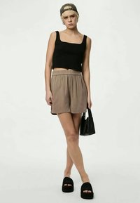 Μαύρο cropped tank top, μπεζ σορτς με ελαστική μέση, μαύρες πλατφόρμες και μια μικρή μαύρη τσάντα. Μοντέλο που φορά καπέλο.