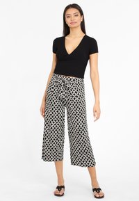 Črn rebrast crop top z globokim V-izrezom, v kombinaciji s hlačami širokega kroja z črno-belimi geometrijskimi vzorci. Črne sandale s trakovi.