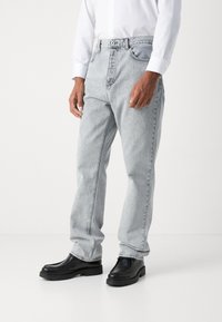 Lys grå denimjeans med en avslappet passform, med klassisk femlommers design og knappelukking, kombinert med svarte slip-on sko.