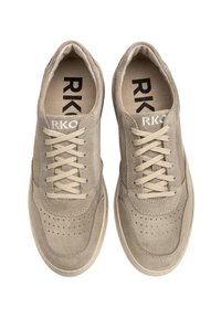 Beige zamšādas sporta apavi ar noapaļotu purngalu, perforētu detaļu, plakaniem beige lencēm un melnu izdrukātu logotipu uz iekšējās zolītes.