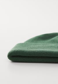 Folded green ribbed knit beanie hat on a white surface, showing the texture and stitching detail.