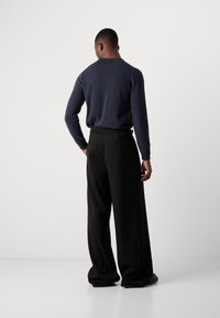Suéter de lana azul marino con cuello, combinado con pantalones de pierna ancha negros. El conjunto presenta un ajuste relajado y texturas suaves.