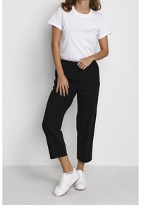 T-shirt blanc à manches courtes associé à un pantalon noir taille haute, avec une coupe droite et des coutures minimales, complété par des baskets blanches.