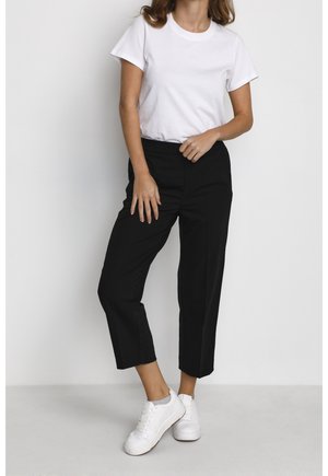 T-shirt blanc à manches courtes associé à un pantalon noir taille haute, avec une coupe droite et des coutures minimales, complété par des baskets blanches.
