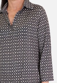 Camisa de manga larga y cuello en colores marino y crema con un patrón geométrico de estrellas; presenta un escote en V y un corte relajado. Textura suave.