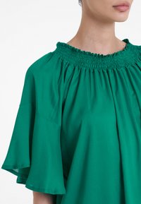 Blusa verde con scollo arricciato e maniche larghe a campana. Tessuto liscio con un design fluido. Nessun motivo o dettaglio visibile.
