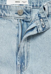 Ljusblå denimjeans med dragkedja och knappstängning, med synliga sömmar och en något fransig tygtextur.