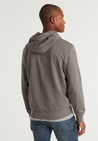 Grijze, pullover hoodie met een trekkoordenkap, ribgebreide boorden en zoom, met een gestructureerde stof. Gecombineerd met blauwe spijkerbroeken.