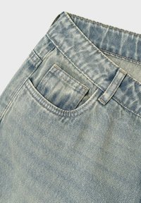 Primer plano de unos pantalones vaqueros de denim azul claro que muestran el bolsillo frontal, el pequeño bolsillo para monedas, el lazo del cinturón y la textura desteñida en la tela.