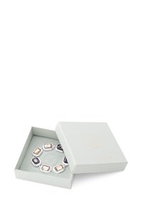 Bracelet en ton argent présentant des pierres multi-facettes rectangulaires et ovales dans des nuances de gris, transparent et rose clair, présenté dans une boîte vert pâle.