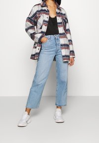 Geruite flanellen overhemd in wit, grijs, rood en marineblauw; zwarte kanten cami-top; high-waisted lichtblauwe jeans; witte sneakers met textuurdetails.