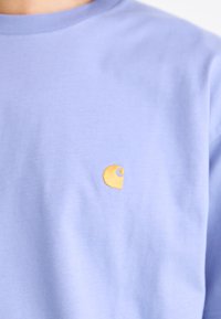 Light purple cotton t-shirt featuring a small, golden embroidered logo on the left side. Crew neck design with short sleeves.