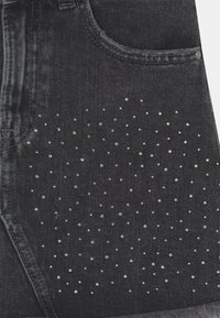 Černé džíny s stříbrnými cvočky uspořádanými v tečkovaném vzoru na oblasti kapes, s klasickým designem pěti kapes.