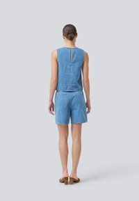 Denim sleeveless top with back keyhole detail, paired with matching denim shorts. Both in light blue, featuring subtle stitching and pockets.