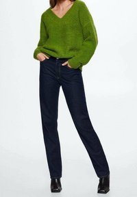 Pull vert à col en V en tissu duveteux assorti à un jean droit bleu foncé et des bottines noires, présentant une coupe décontractée et un design minimaliste.