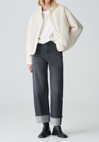 Kurtka bombka w kolorze kremowym, pikowana, noszona na białej bluzce, połączona z ciemnoniebieskimi, skróconymi szerokimi jeansami z szarymi mankietami oraz czarnymi botkami za kostkę.