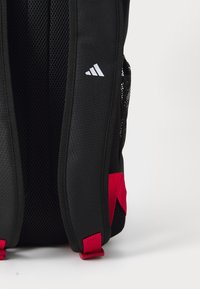 Svart ryggsekk med nettingpaneler, røde detaljer og en hvit logo. Designet med justerbare stropper og mesh-lommer på siden for praktisk bruk.