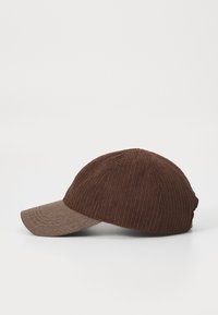 Casquette en tissu côtelé marron avec une visière brun clair. Elle présente une couronne arrondie et un bord incurvé, mettant en valeur un extérieur texturé.
