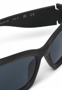 Schwarze Sonnenbrille mit matter Oberfläche, leicht geschwungen, mit dunklen Gläsern und Zertifizierungsmarkierungen an den Schläfen.