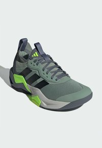 Chaussure de sport Adidas avec un upper en mesh vert, des rayures noires, des accents gris et une semelle texturée avec un détail de talon vert vif.
